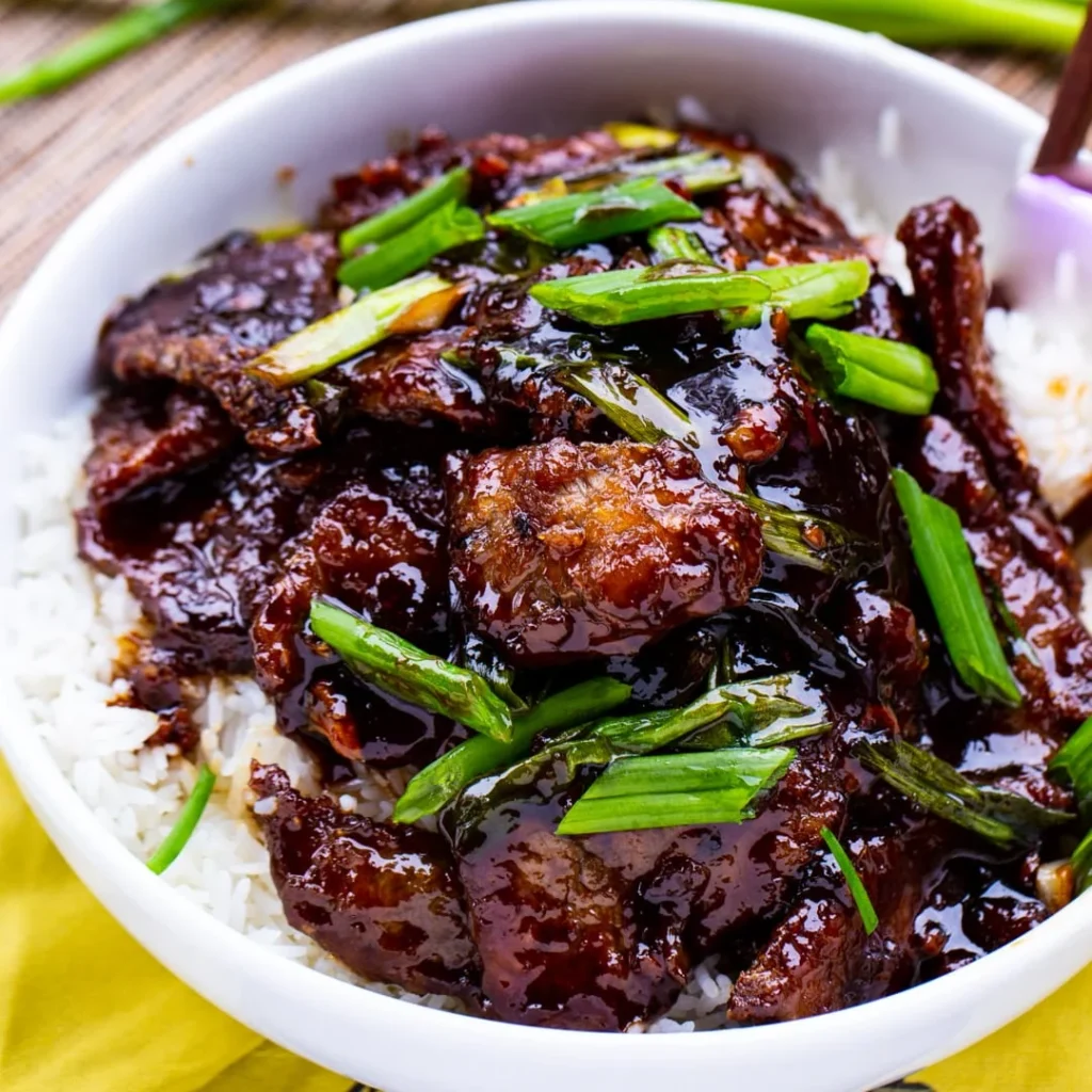 mongolian beef recipe: A delicious plate of Mongolian beef with tender beef slices in a glossy sweet-savory sauce, served over rice and garnished with green onions and sesame seeds.